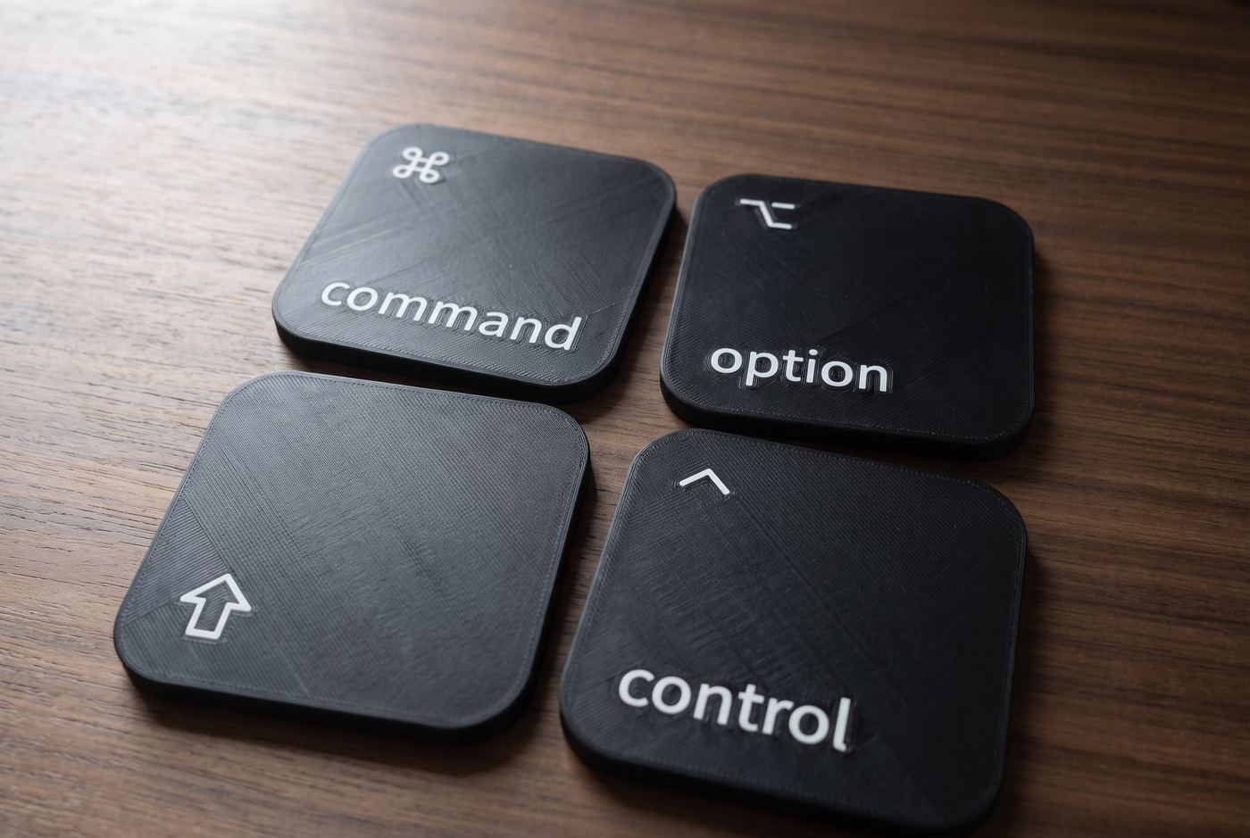 The four coasters two by two on a walnut desk: command, option, shift and control.