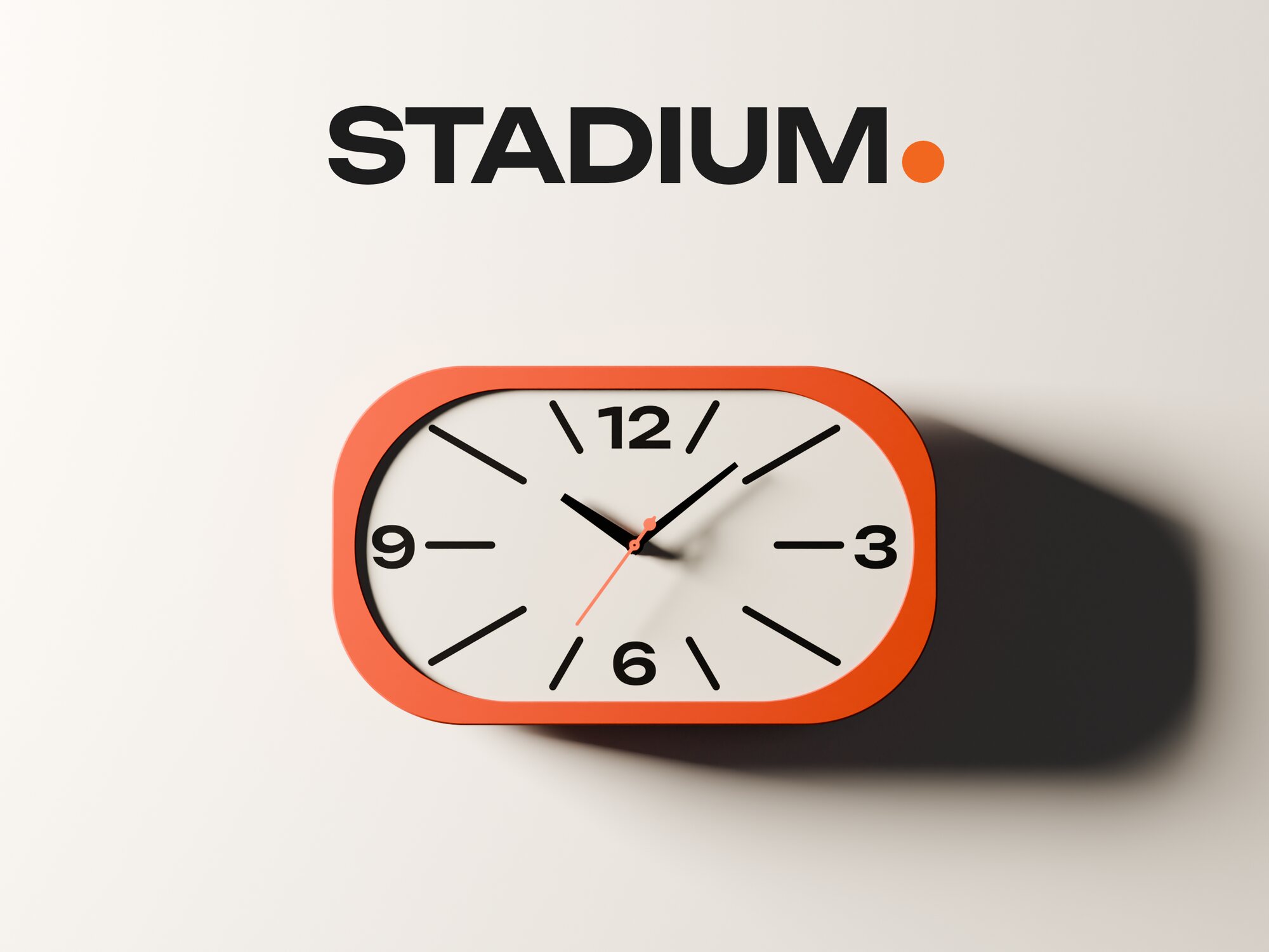 The Stadium wall clock straight on against a pale wall, the word STADIUM above it with an orange dot.